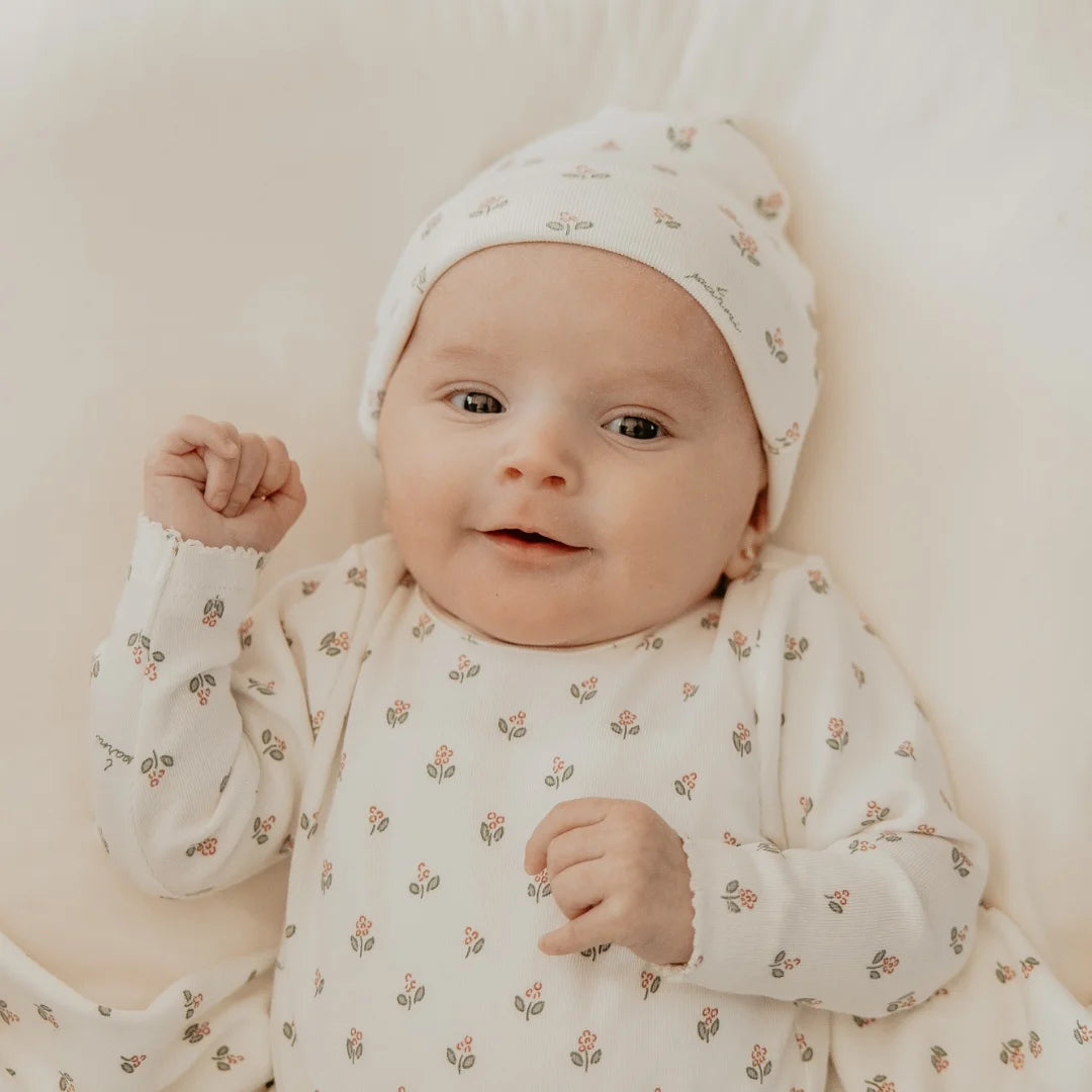 Baby wearing a floral outfit and hat on a soft surface
