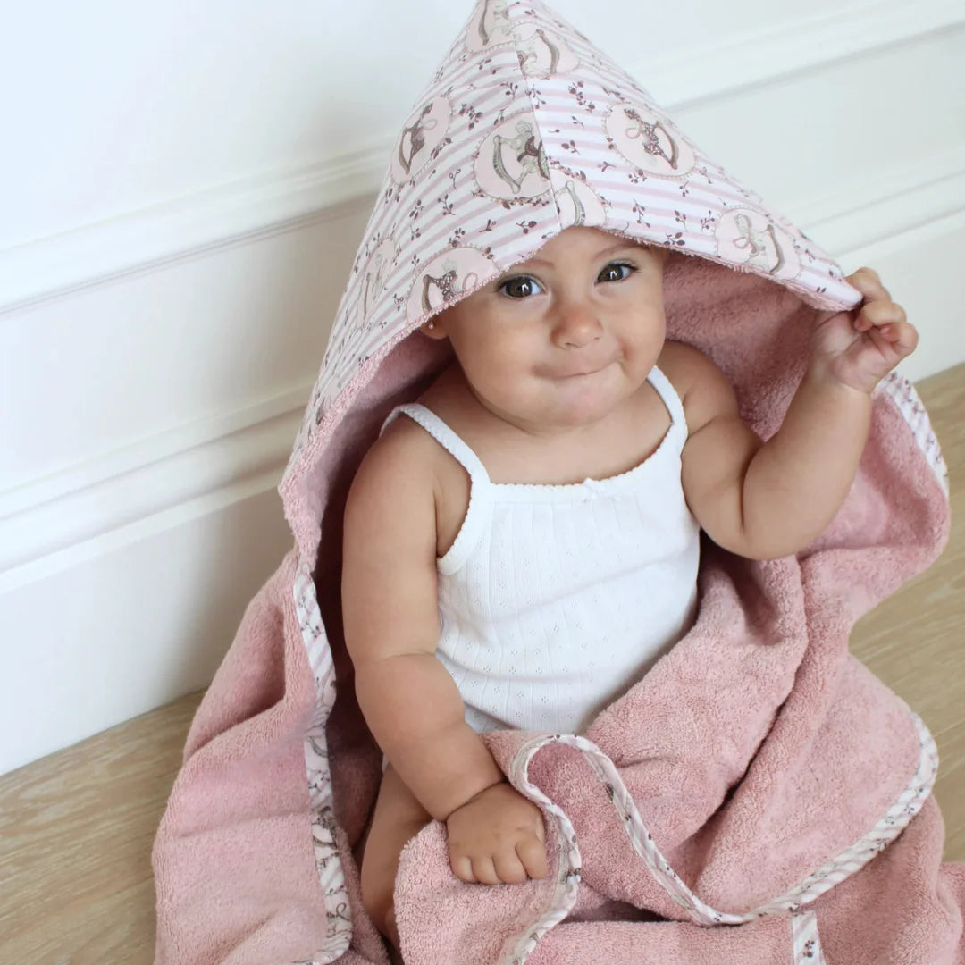 A front view of the soft rose-colored hooded bath towel with a rocking horse design by Little Threads.