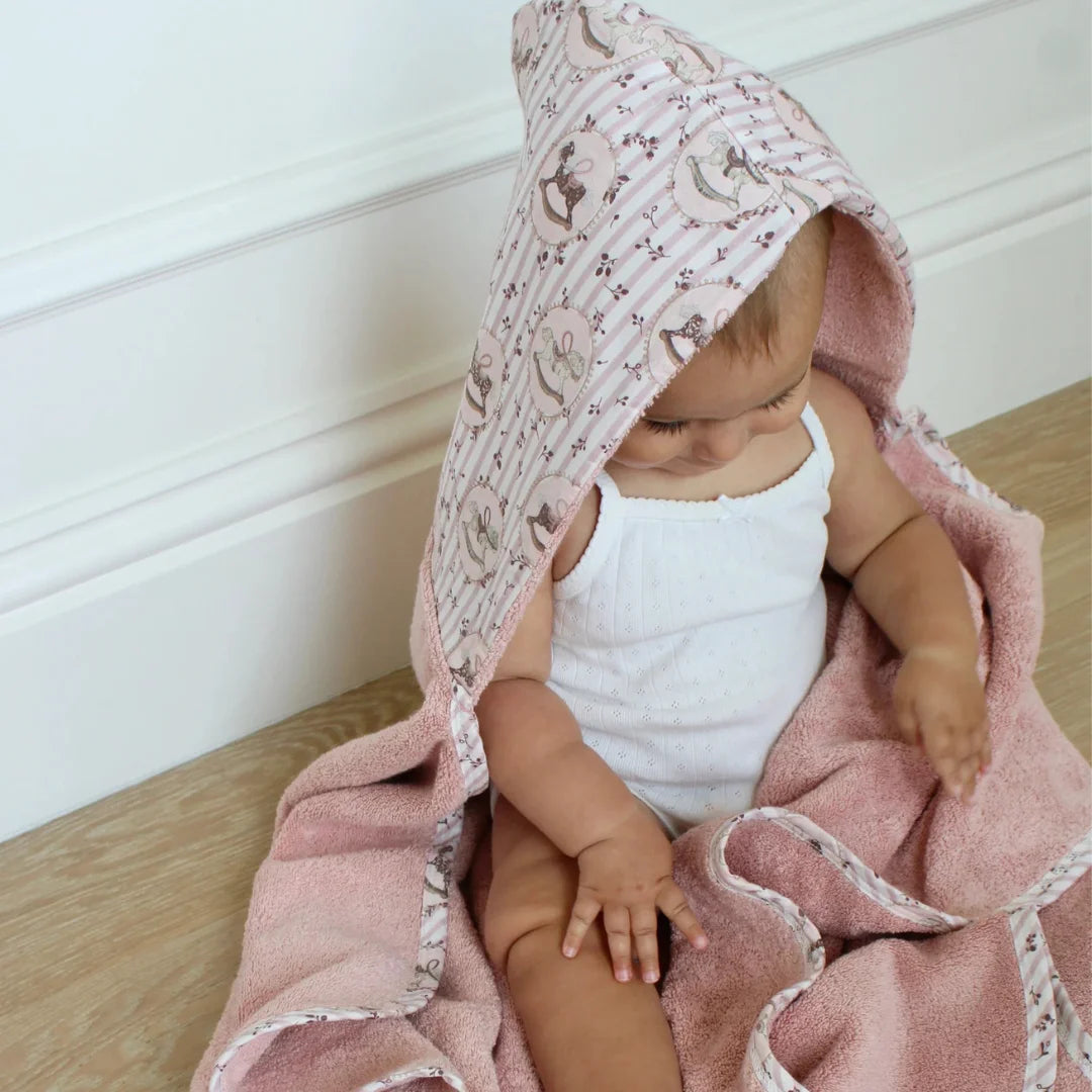 A happy baby wrapped in the Little Threads rocking horse hooded bath towel.