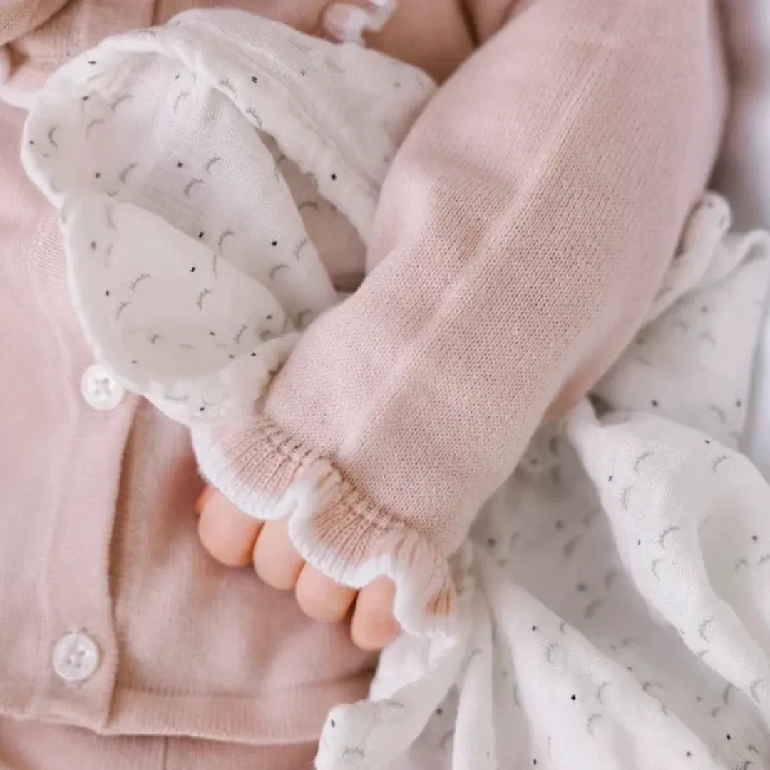 A newborn infant swaddled peacefully under the Livly white blanket in a luxury nursery