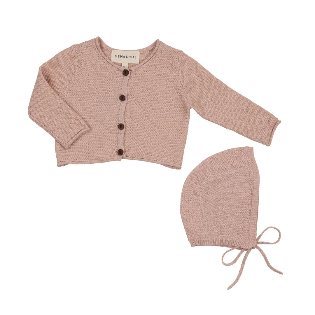 A flat-lay view of the Mema Knits pale pink cropped knit cardigan and bonnet set.