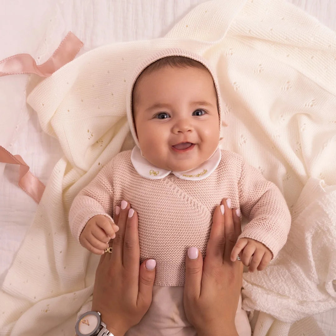An infant styled in the Mini Label pink wrap cardigan and bonnet during a portrait session.
