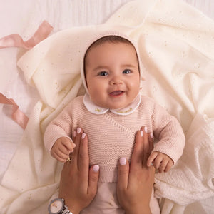 An infant styled in the Mini Label pink wrap cardigan and bonnet during a portrait session.