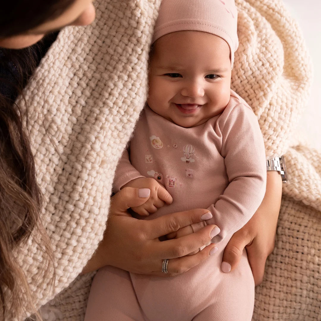 A newborn baby wearing the Mini Label pink footie comfortably during a quiet nap.