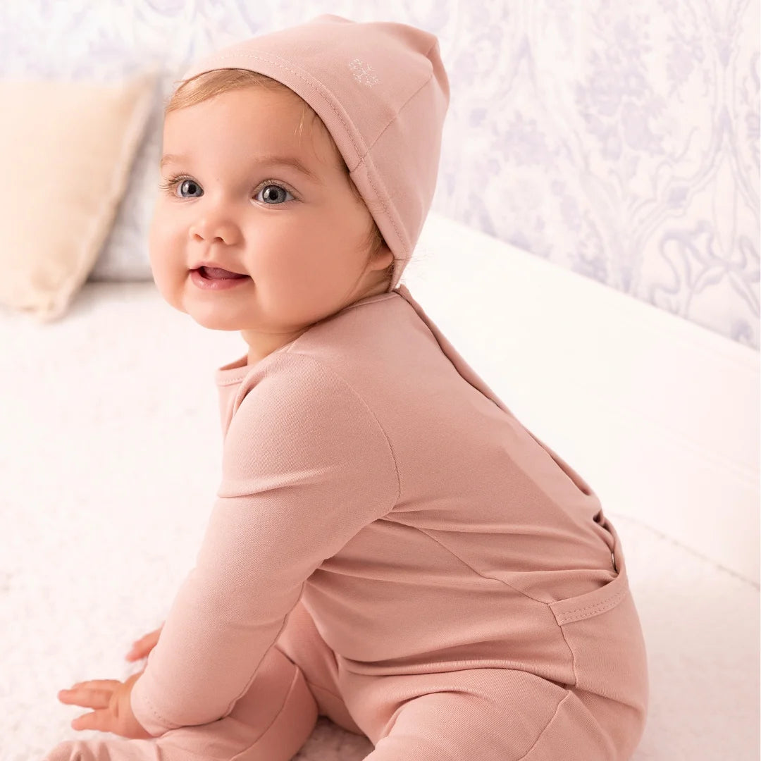 A newborn baby wearing the Mini Label pink footie comfortably during a quiet nap.