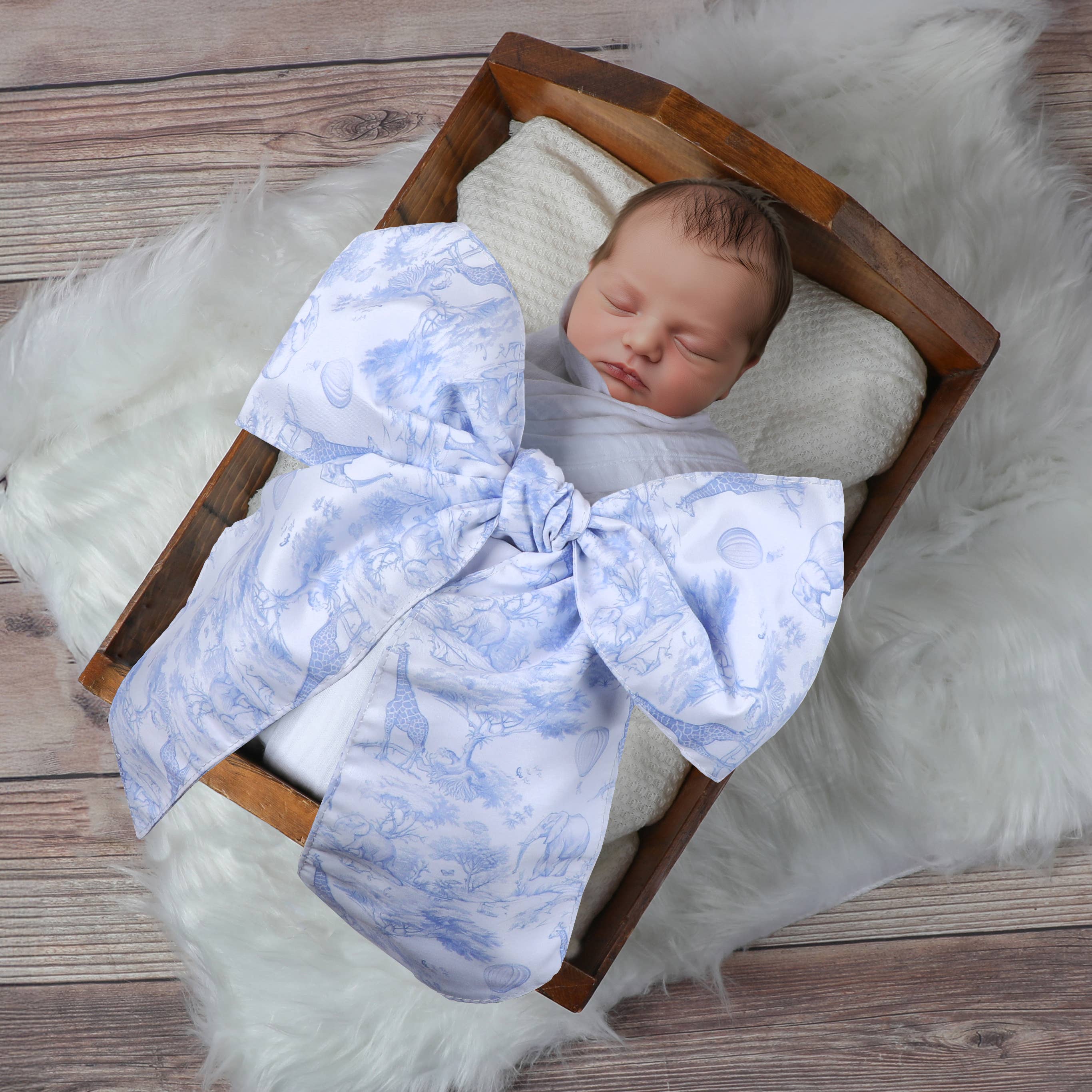 A breathtaking newborn swaddle sash featuring a refined blue Safari Toile de Jouy print and an authoritative, architectural oversized bow.