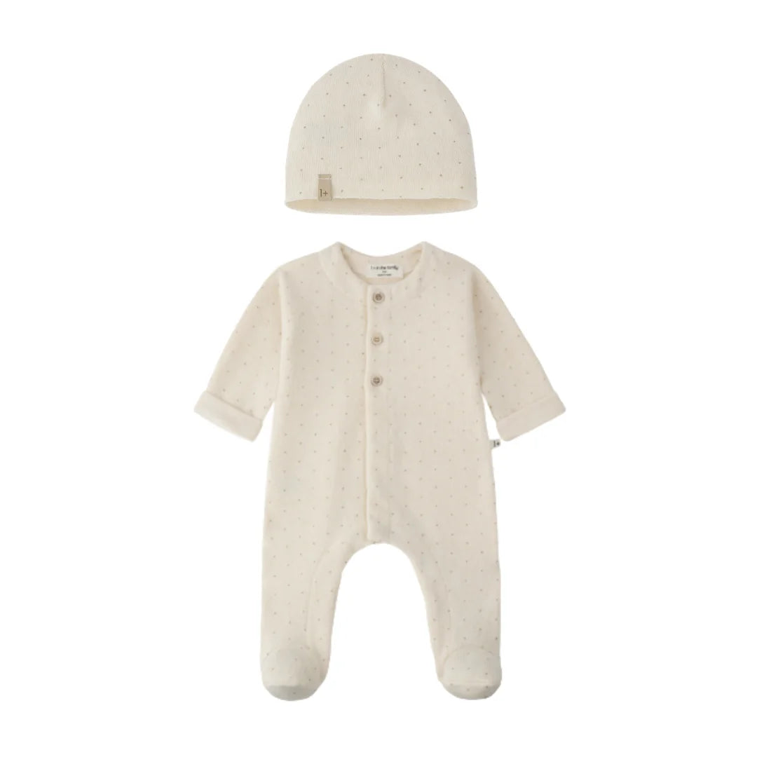A baby sleepwear set featuring a long-sleeve footed sleeper and a matching beanie hat, both in a warm cream color with tiny light brown polka dots. The sleeper has three front buttons and a small fabric brand tag on the inside neck.