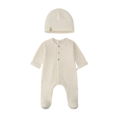 A baby sleepwear set featuring a long-sleeve footed sleeper and a matching beanie hat, both in a warm cream color with tiny light brown polka dots. The sleeper has three front buttons and a small fabric brand tag on the inside neck.