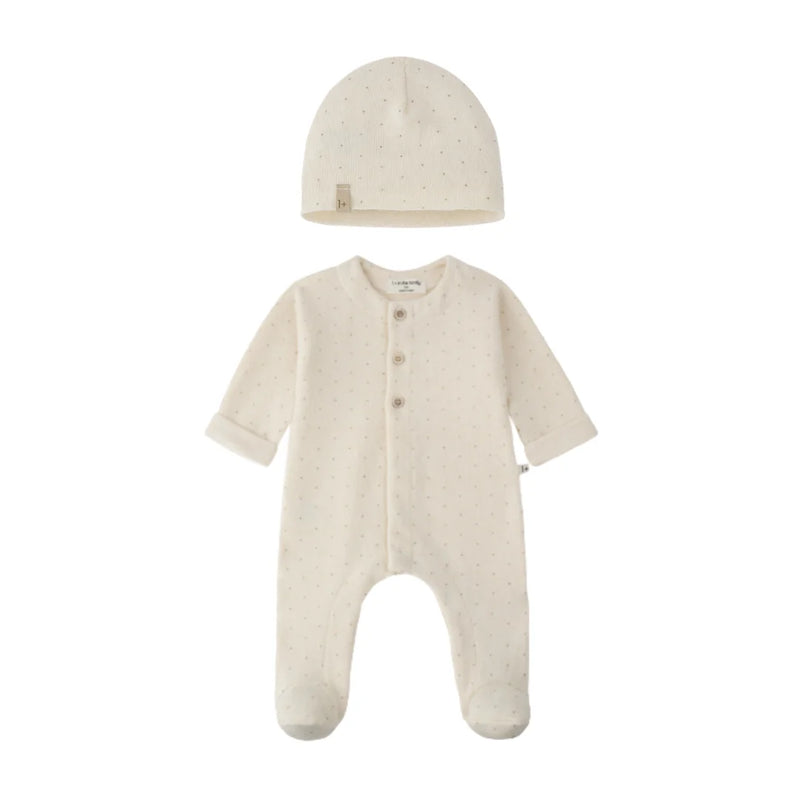 A baby sleepwear set featuring a long-sleeve footed sleeper and a matching beanie hat, both in a warm cream color with tiny light brown polka dots. The sleeper has three front buttons and a small fabric brand tag on the inside neck.