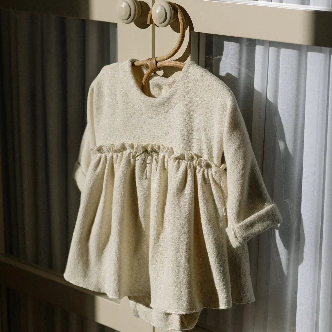 Beige baby dress hanging on a wooden hanger against a neutral background