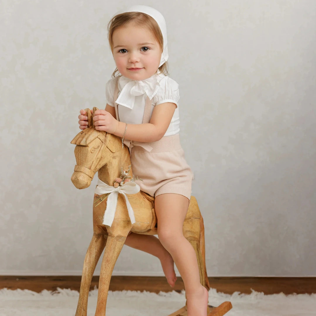 Child sitting on a wooden rocking horse against a plain background
