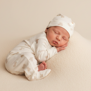 Newborn baby sleeping on a beige blanket wearing a matching outfit and hat.