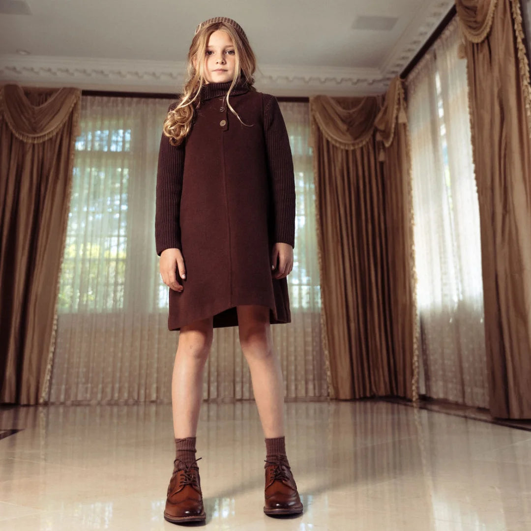 A toddler wearing the Pompomme brown wool dress set during a family gathering.