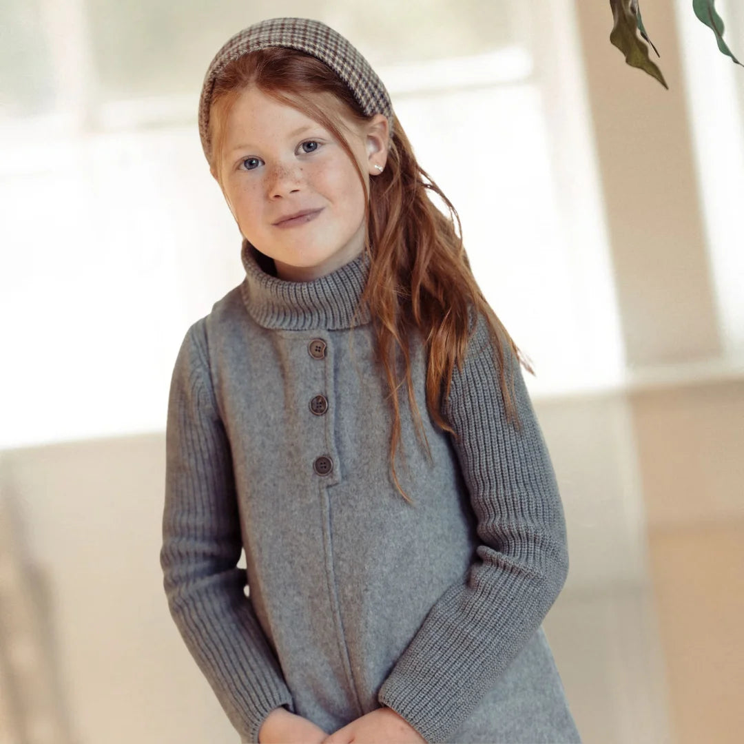 A toddler wearing the Pompomme grey wool dress set during a family gathering.