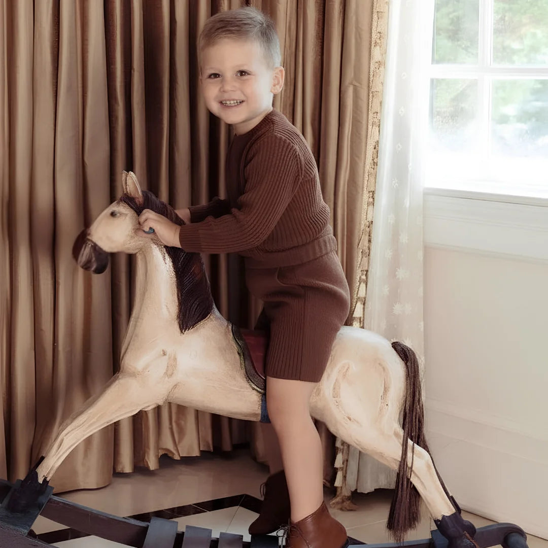 A toddler wearing the Pompomme brown wool bermuda set during a family gathering.