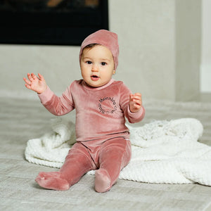 An infant comfortably wearing the Pouf pink velour footie sleeper.