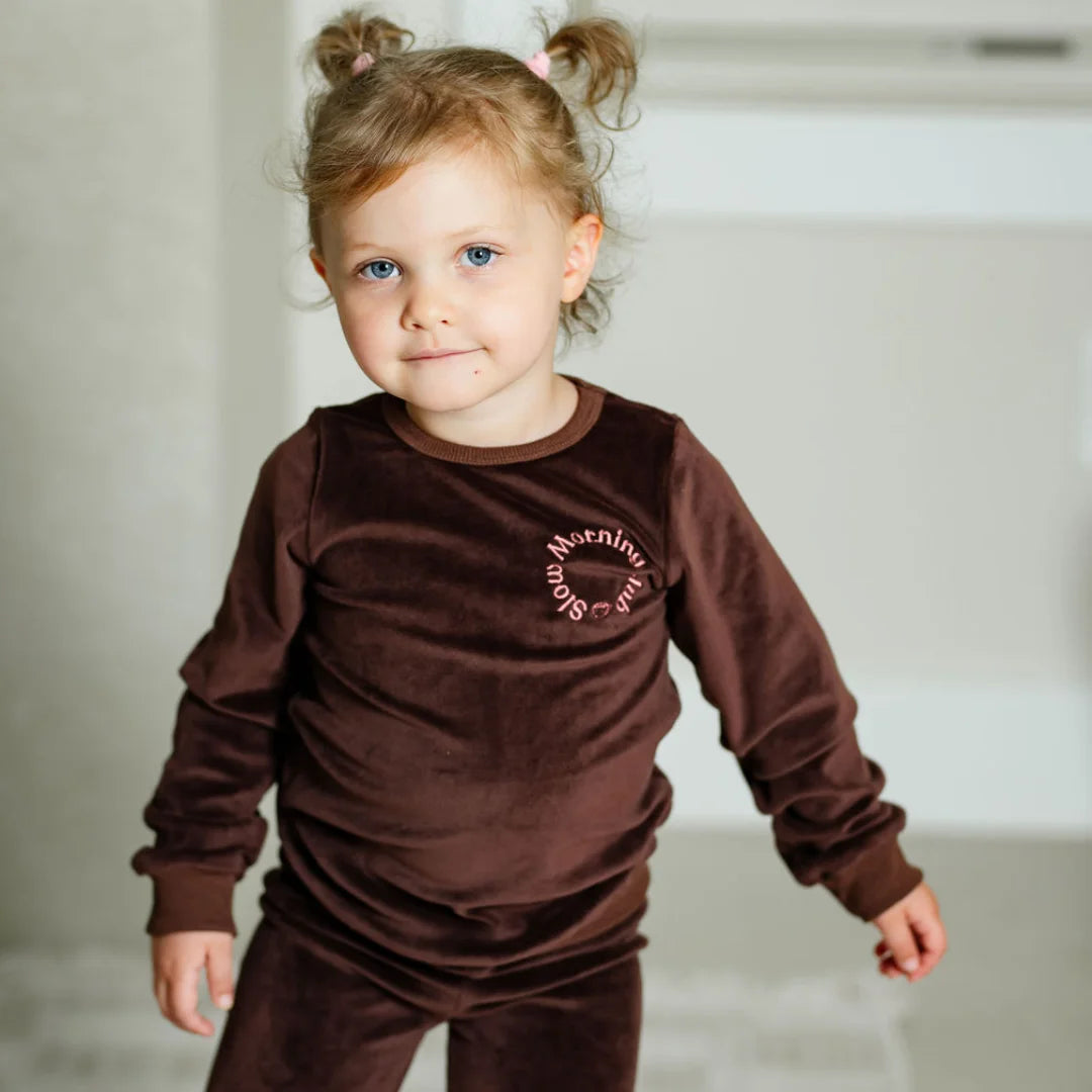 A child wearing the Pouf brown velour pajamas comfortably during a cozy morning at home