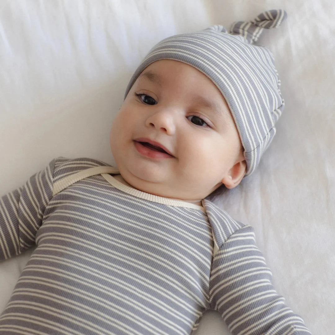 An infant resting peacefully while wearing the Quincy Mae slate microstripe knotted gown and hat.