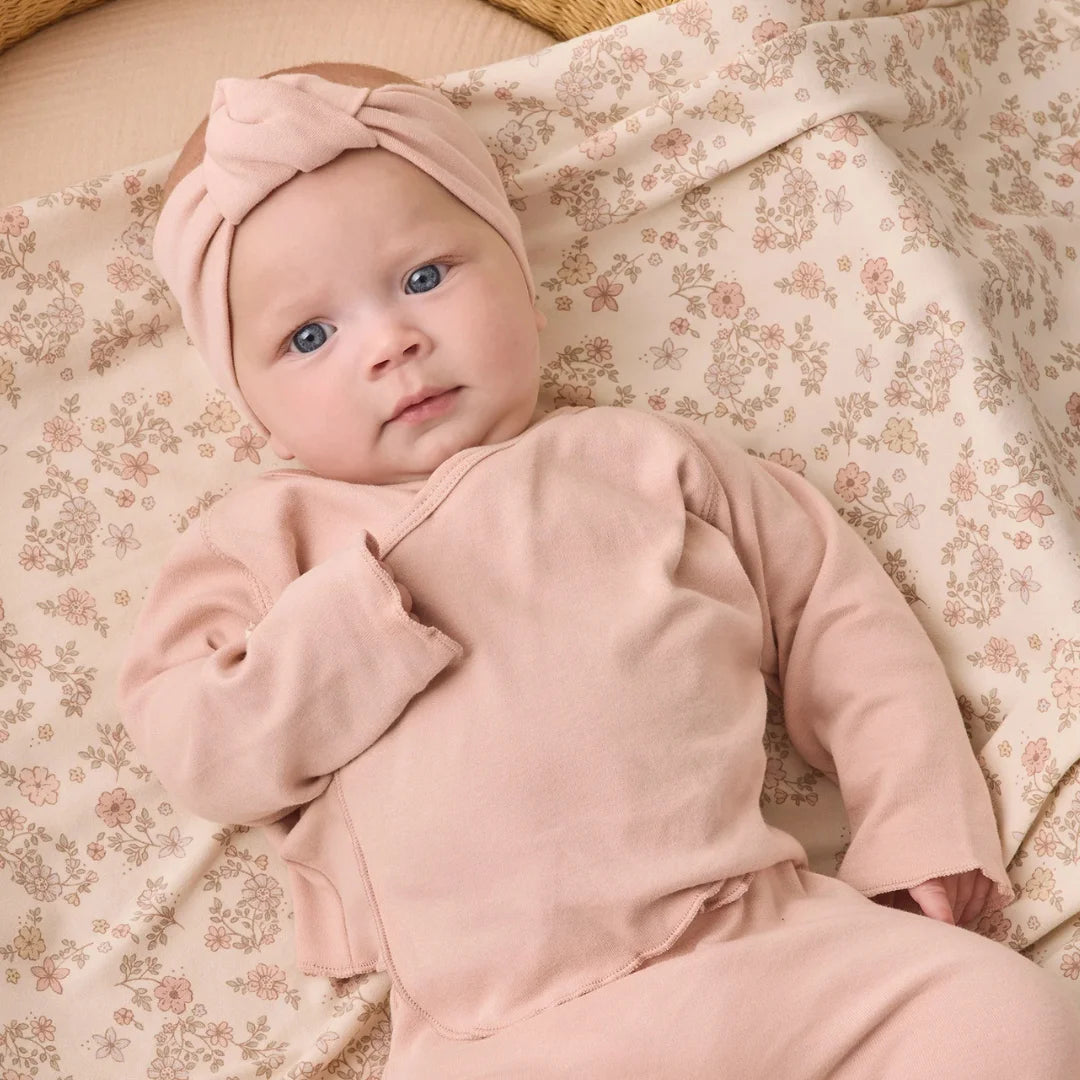 An infant wearing the Quincy Mae dusty rose knotted headband comfortably during an outing.