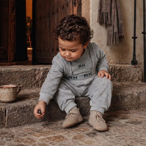 A happy baby boy wearing the gray and green RetroKid overalls set.