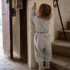A baby girl sitting and playing comfortably in the RetroKid gray and red overalls outfit back