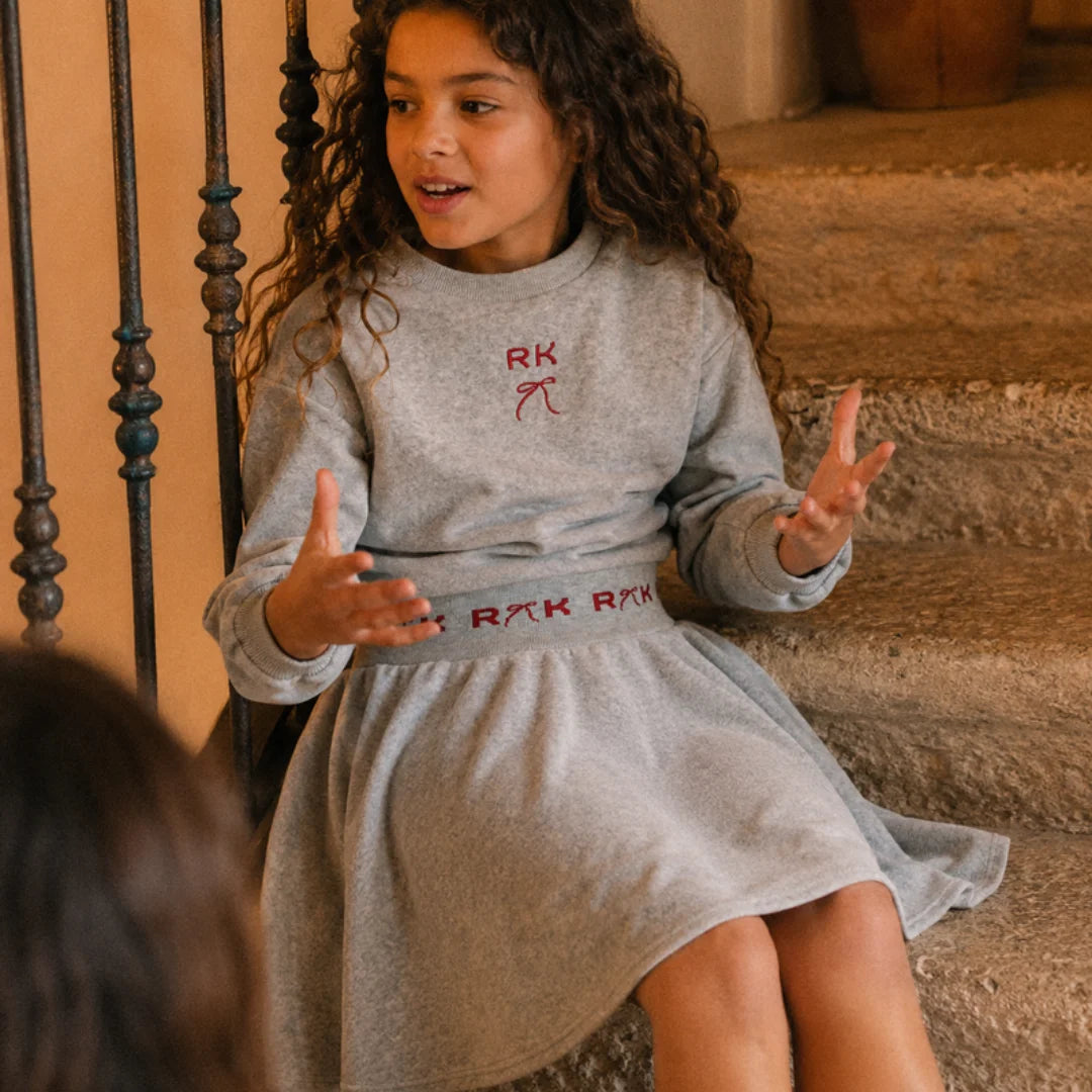 A girl sitting while comfortably wearing the gray and red RetroKid Reese scuba top.