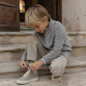 Child sitting on stone steps tying a shoe, wearing the cozy gray RetroKid velour zip-up.