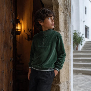 A boy the cozy green velour RetroKid zipper sweatshirt over a t-shirt.