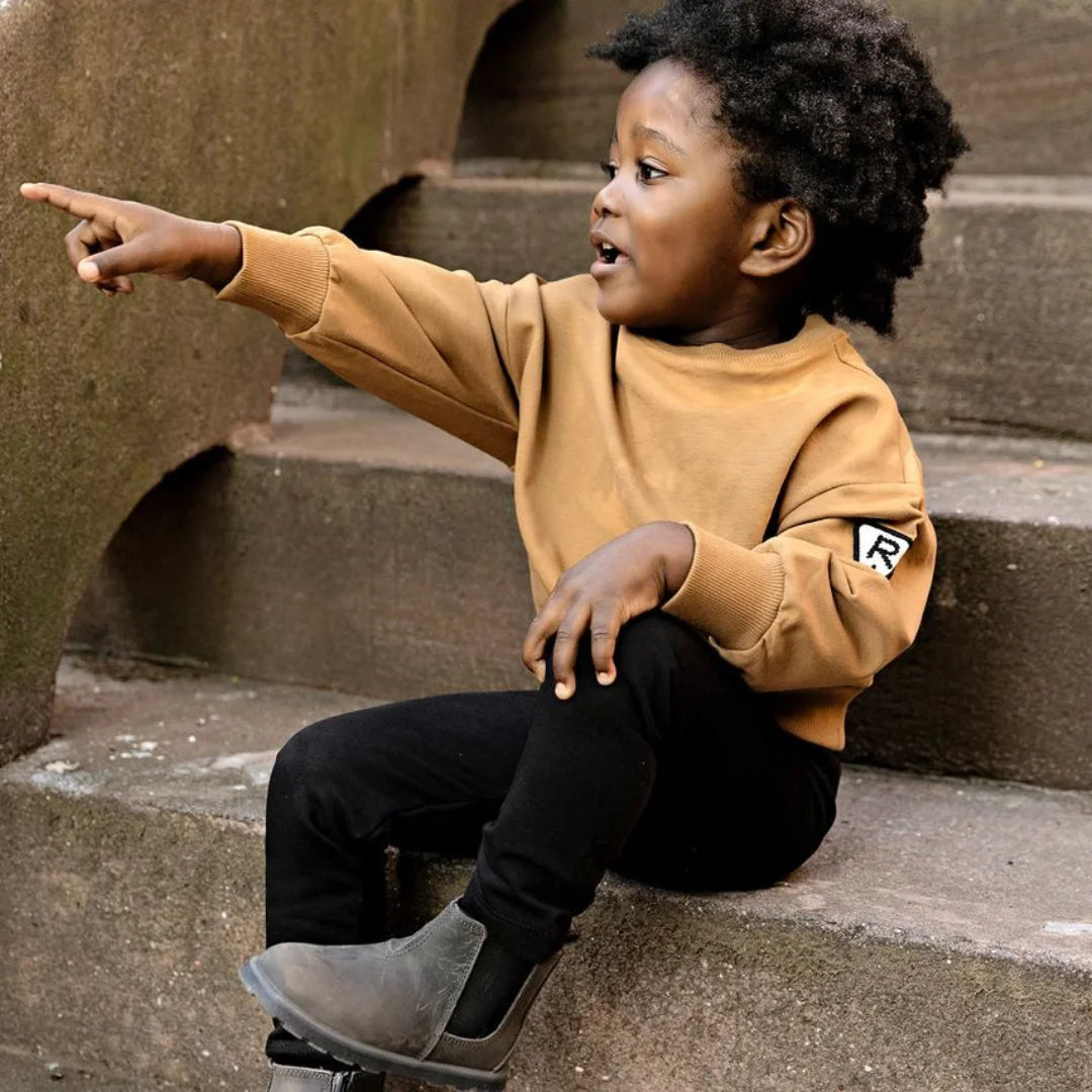 A child wearing the Rooie and Friends caramel sweatshirt during an outdoor playground adventure.