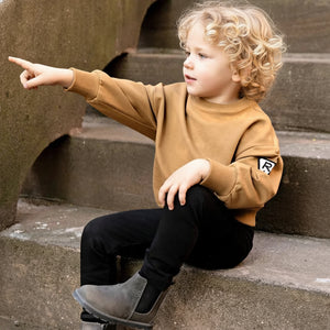 A child wearing the Rooie and Friends caramel sweatshirt during an outdoor playground adventure.