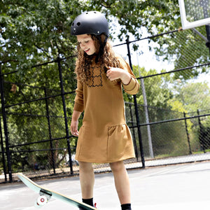 A child wearing the Rooie and Friends caramel/black dress during a sunny outdoor outing.