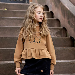 A child wearing the Rooie and Friends caramel/black sweatshirt during an outdoor playground adventure.