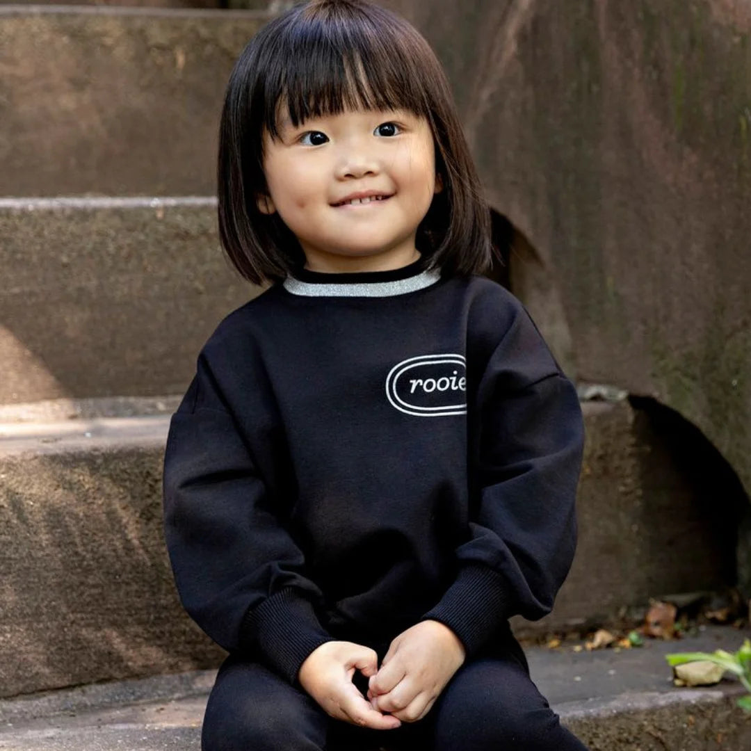 A child wearing the Rooie and Friends black and silver sweatshirt during an outdoor playground adventure.