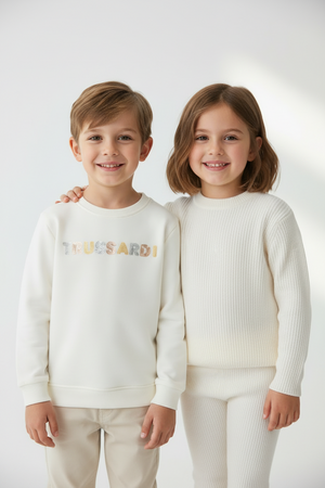 Two children wearing white sweaters with a brand logo on a light background